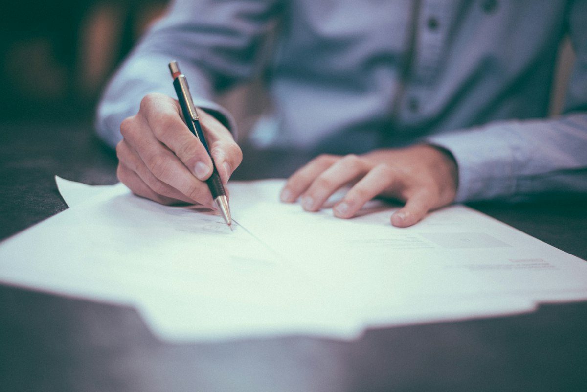 A person signing paperwork with a pen, representing invoice documents.